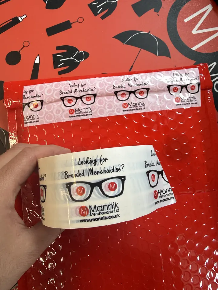 Mannik branded packing tape on a red mailer bag printed with merchandise icons